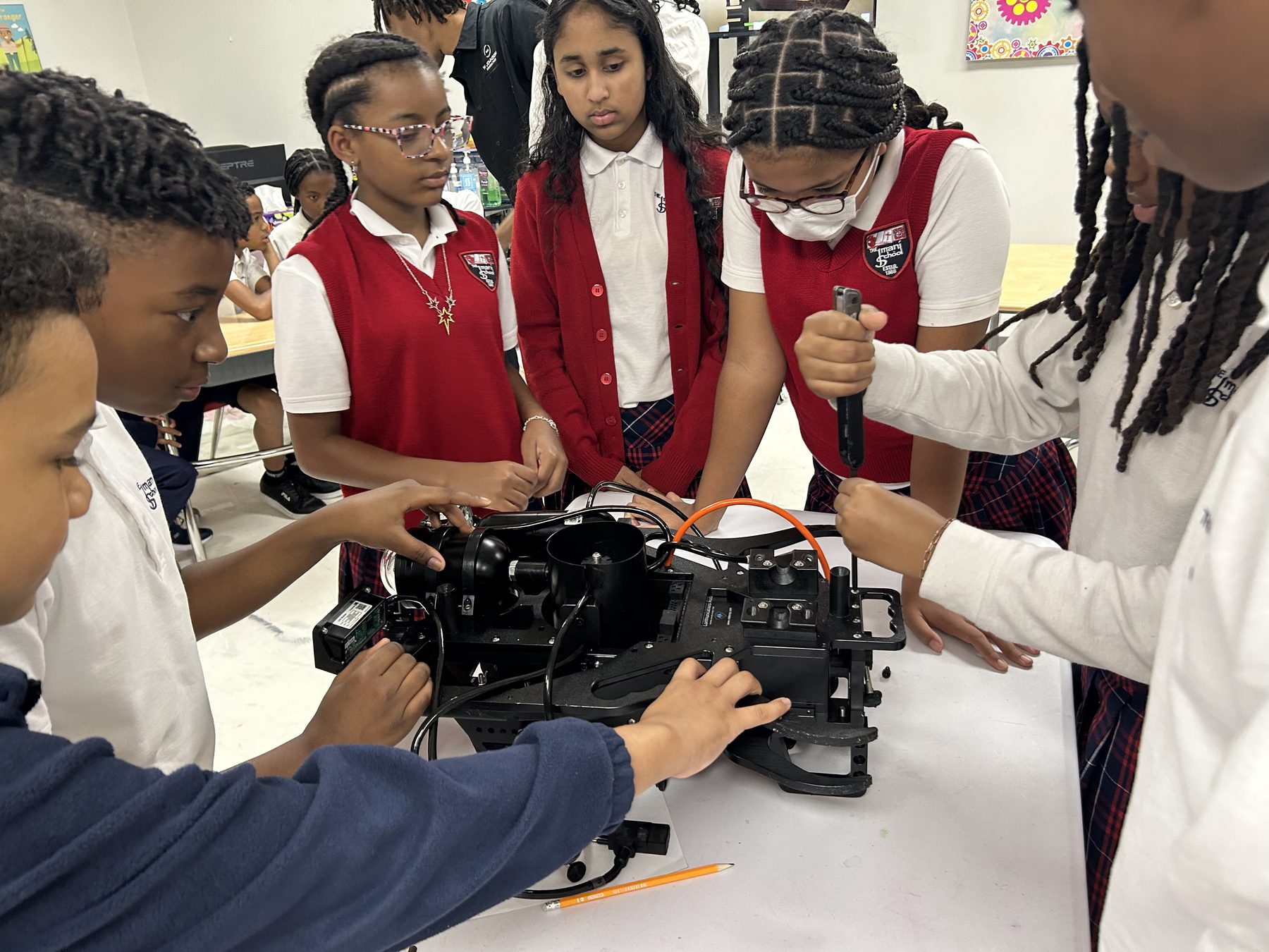 Imani School students gathered around a laptop and drone components during a STEM lesson.