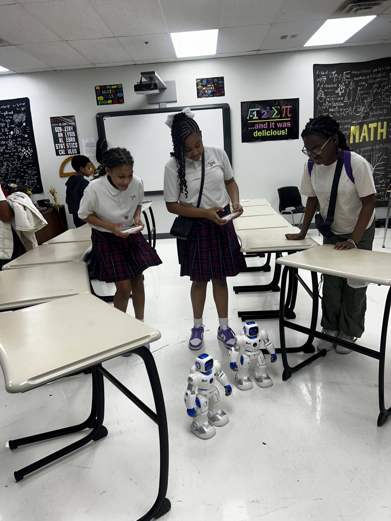 Imani School students programming two humanoid robots in a classroom.